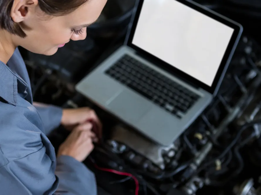 sécurité véhicule : Une femme avec un PC posé sur un moteur travaillant dessus